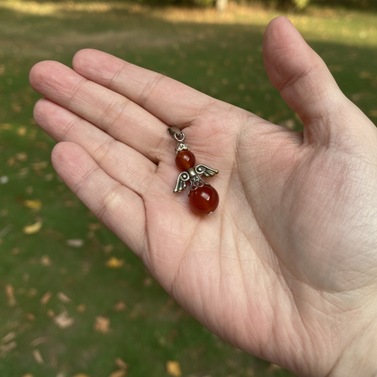 engelenhanger van rode agaat in de hand met grassige achtergrond