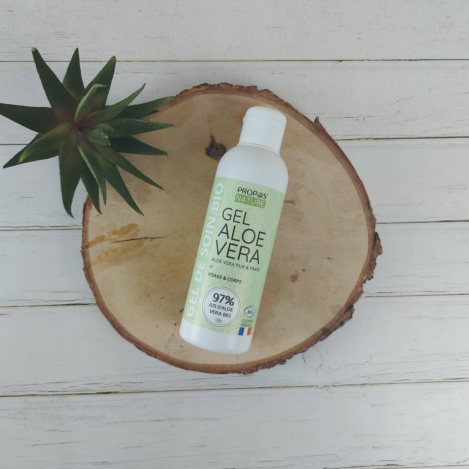 flesje aloe vera gel van propos' nature liggend op een schijf hout met plantje
