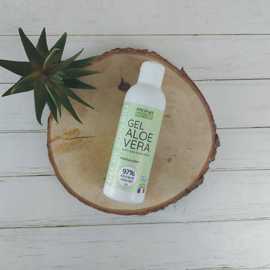 flesje aloe vera gel van propos' nature liggend op een schijf hout met plantje