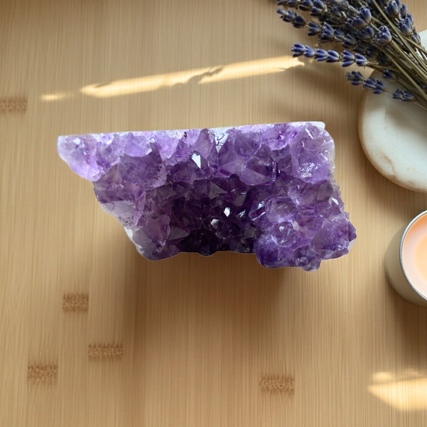 amethist cluster op een houten tafel met gedroogde lavendel en een kaarsje