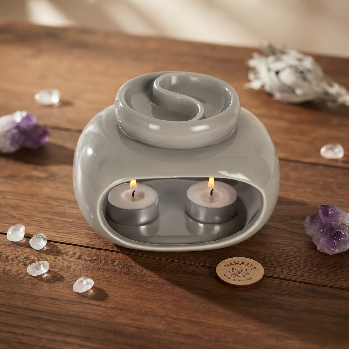 grijze keramieke yin-yang brander op een houten tafel met wat kleine kristallen errond