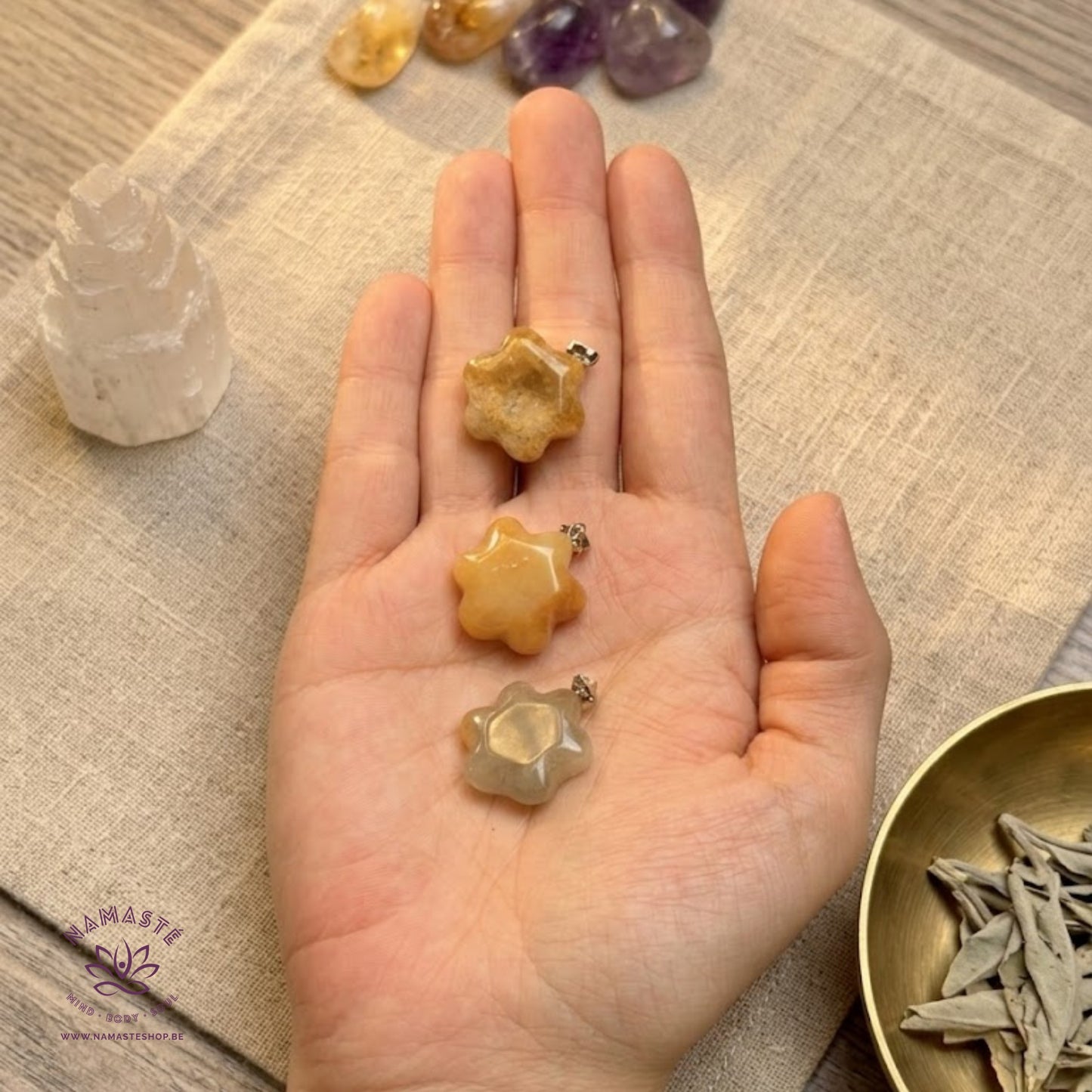 gele jade hangers op een hand met een linnen doek onder en seleniet, trommelstenen en gedroogde kruiden