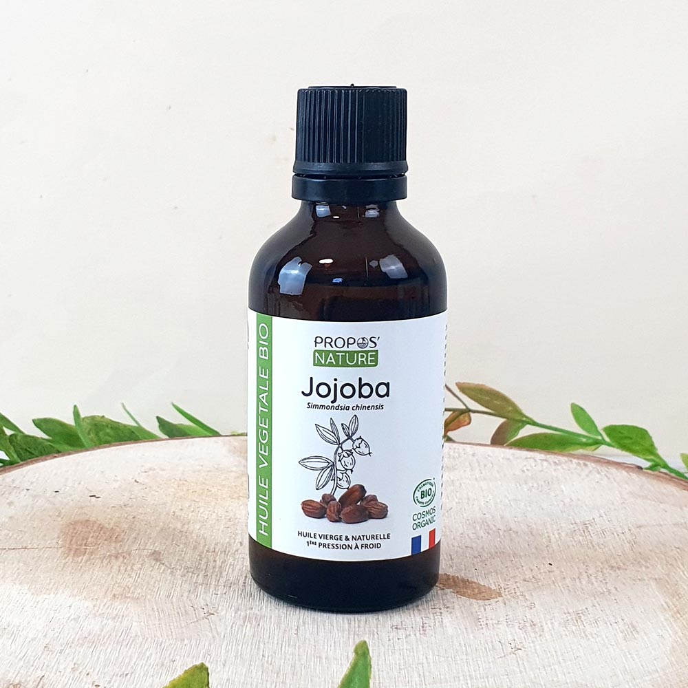 flesje jojoba olie op een houten schijf en wat takjes errond
