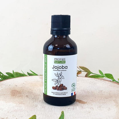 flesje jojoba olie op een houten schijf en wat takjes errond