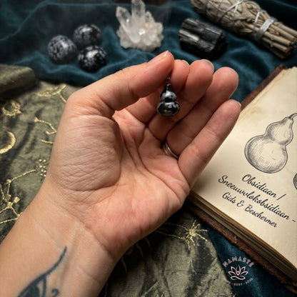 sneeuwvlok obsidiaan hanger in de hand met een spirituele achtergrond met kristallen, een boek en smudge