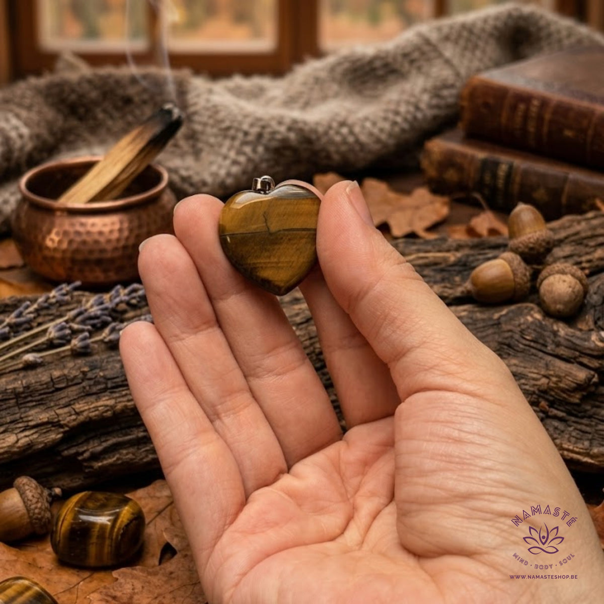 Tijgeroog hart hanger in de hand met op de achtergrond lavendel, eikels en smudge